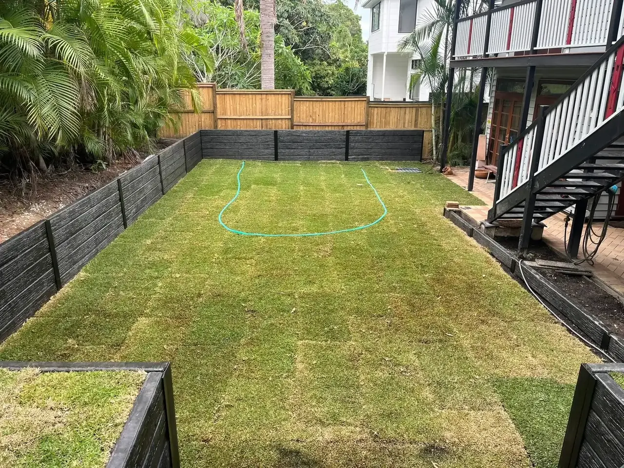 Charcoal concrete retaining walls bordering a backyard lawn