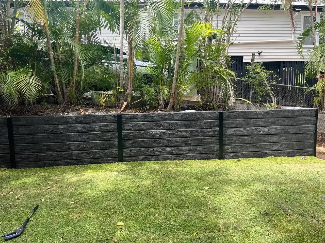 Charcoal concrete sleeper retaining wall along a backyard lawn