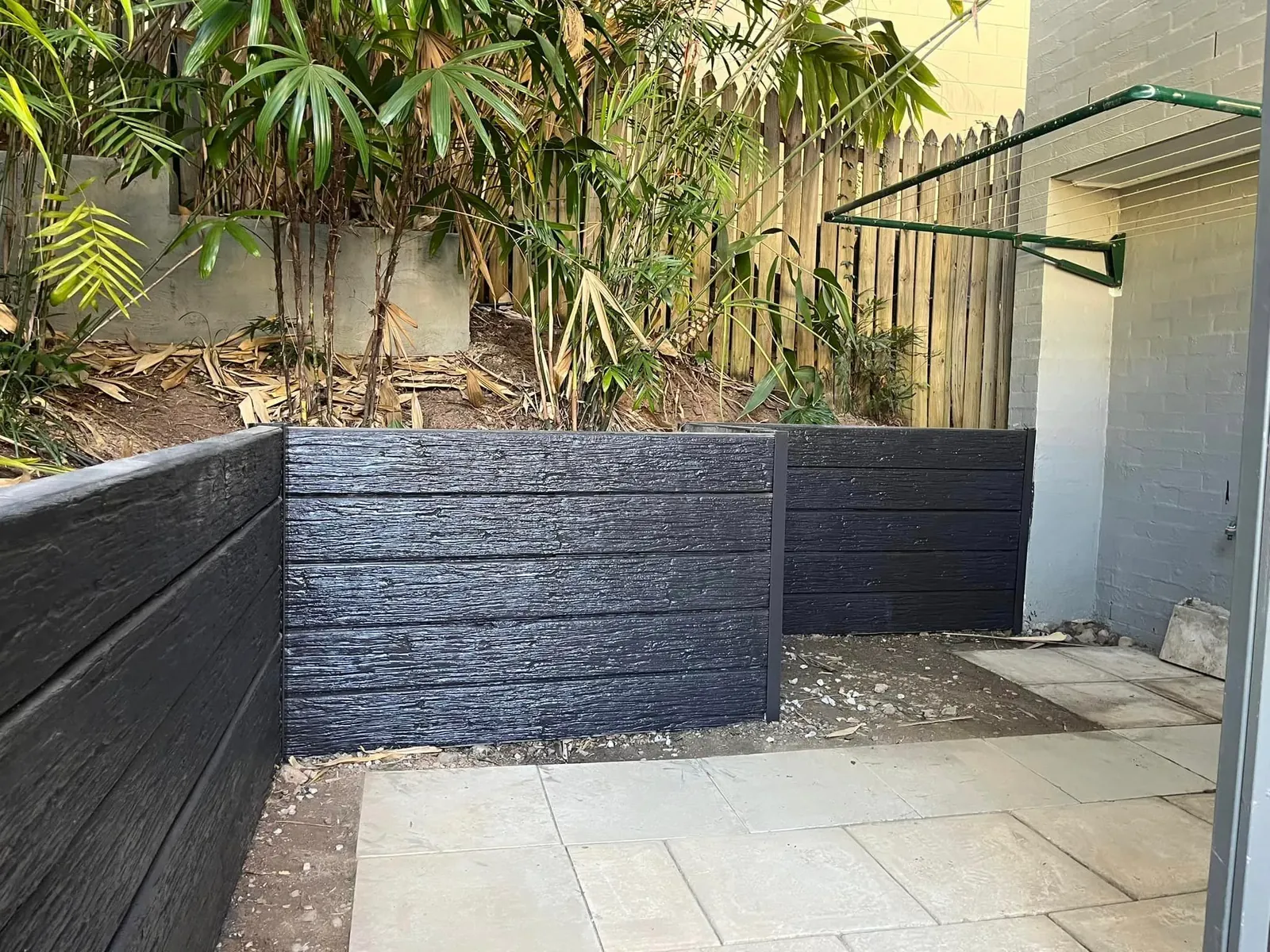 Charcoal timber-look concrete retaining wall beside a paved area