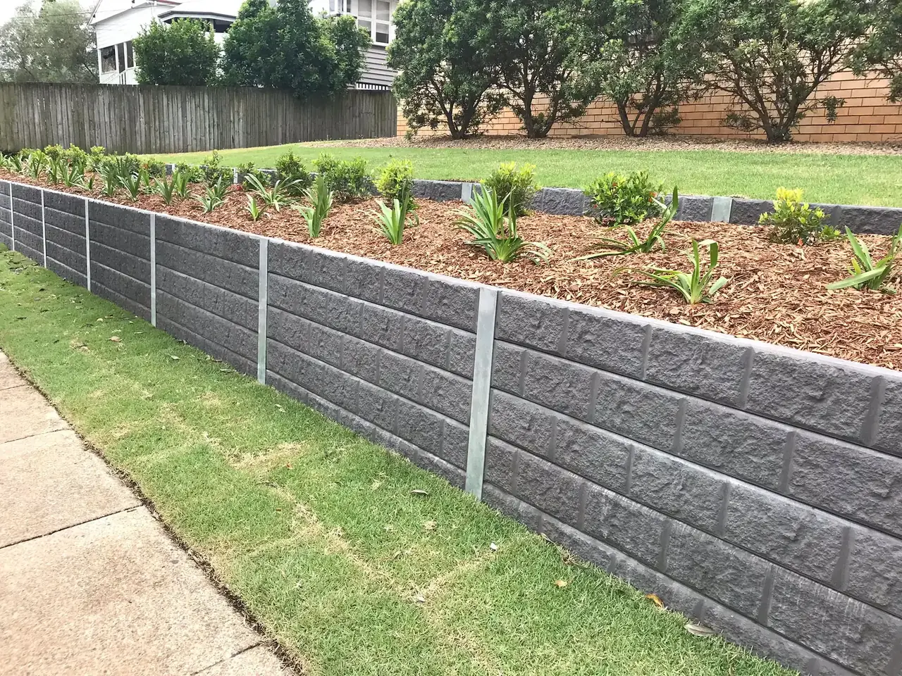 Grey textured concrete retaining wall along a garden bed and footpath