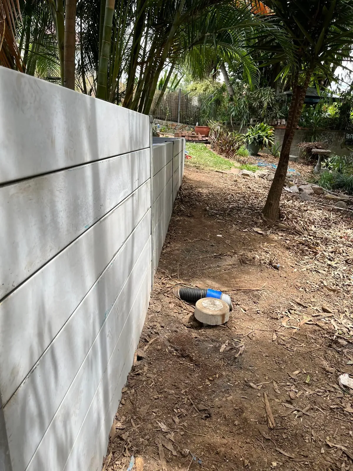 Tall grey concrete sleeper retaining wall along a garden boundary