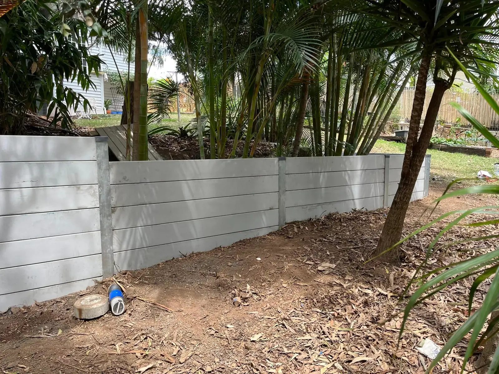 White concrete sleeper retaining wall in a leafy backyard