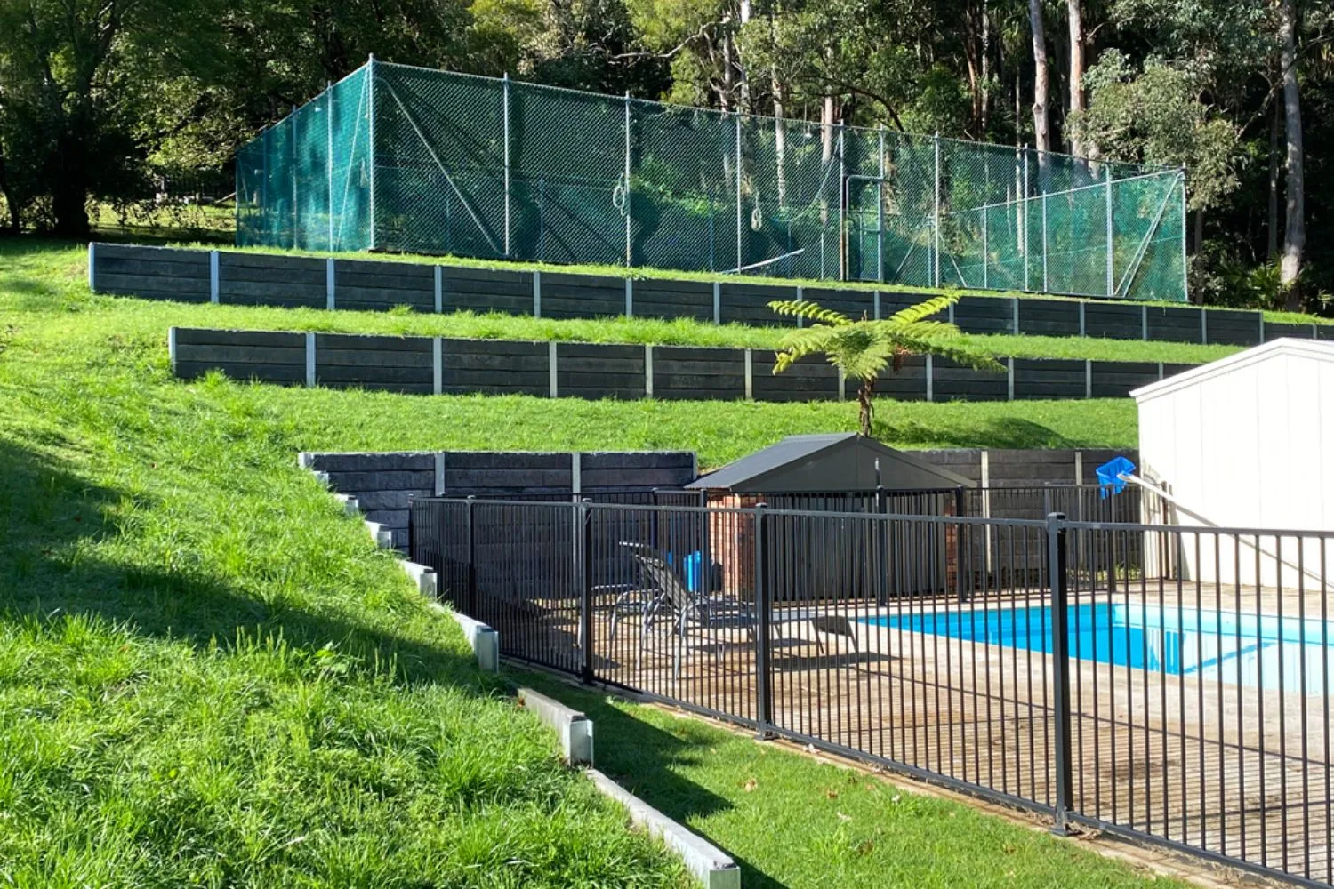 Tiered concrete sleeper retaining walls on a sloping block above a pool