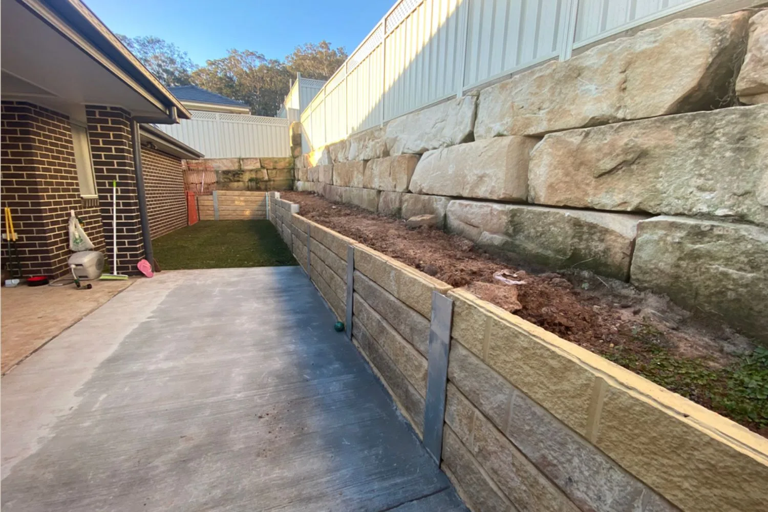 Concrete sleeper retaining wall lining a side path beside sandstone blocks