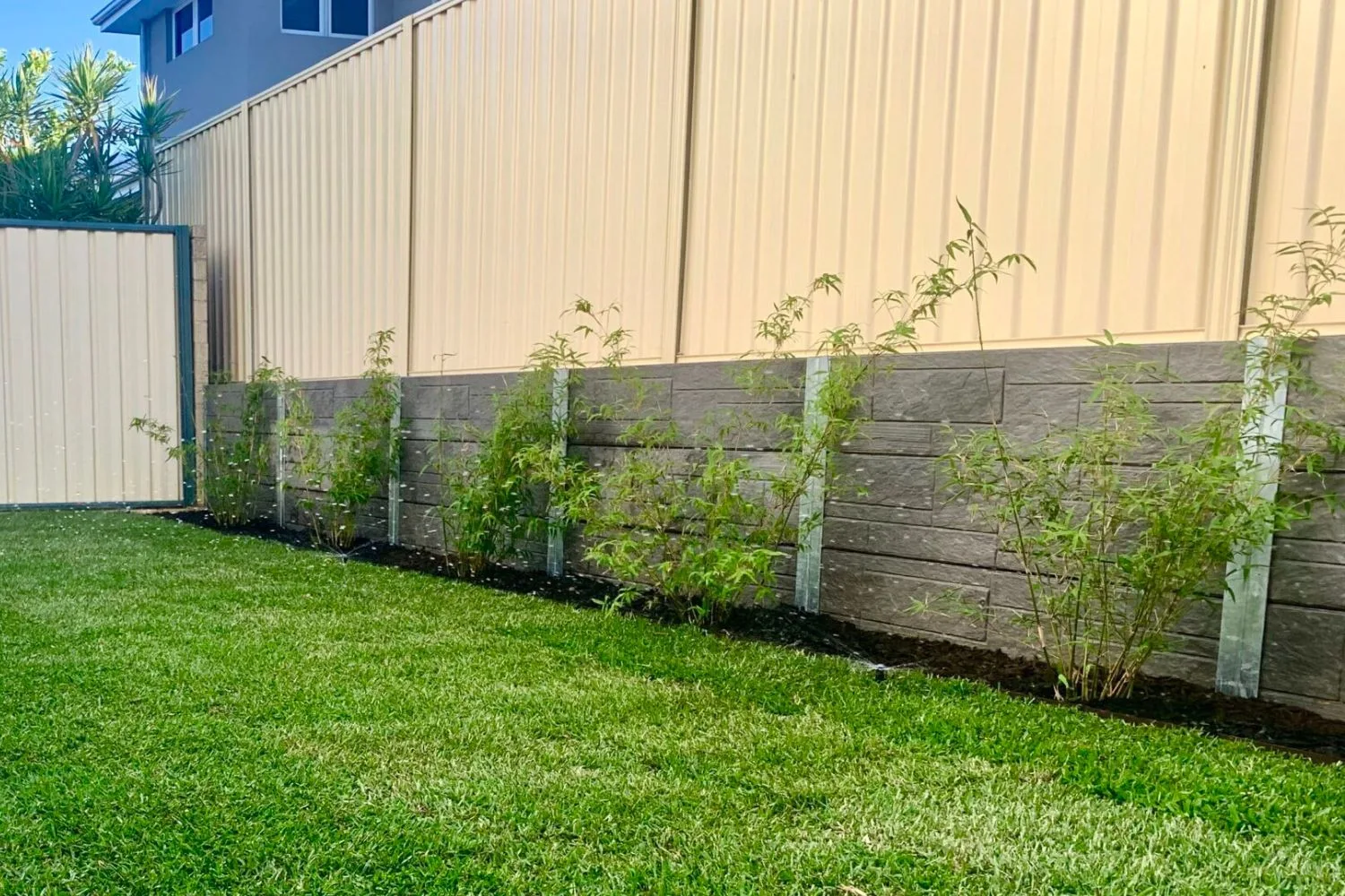 Concrete sleeper retaining wall along a colorbond boundary fence with new plants