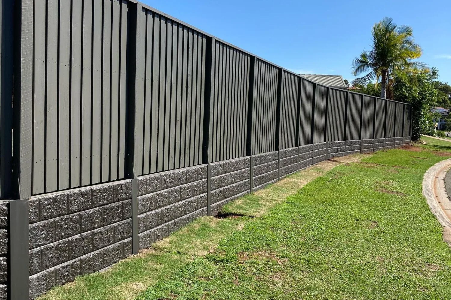 Textured concrete sleeper retaining wall below a black boundary fence