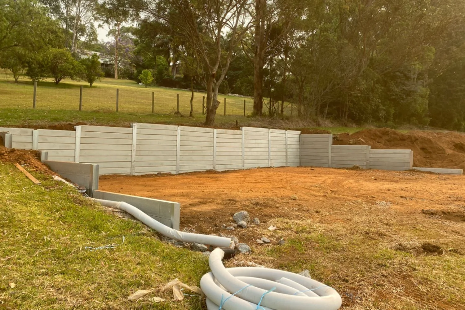 Concrete sleeper retaining wall under construction with drainage pipe