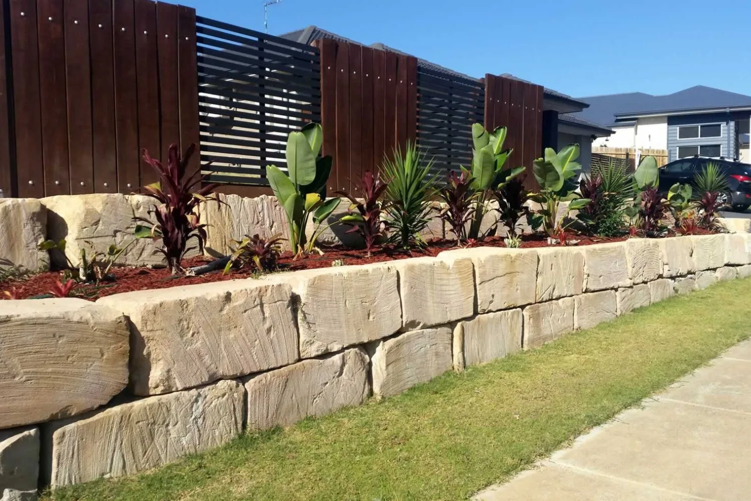 Sandstone block retaining wall with garden plants along a footpath