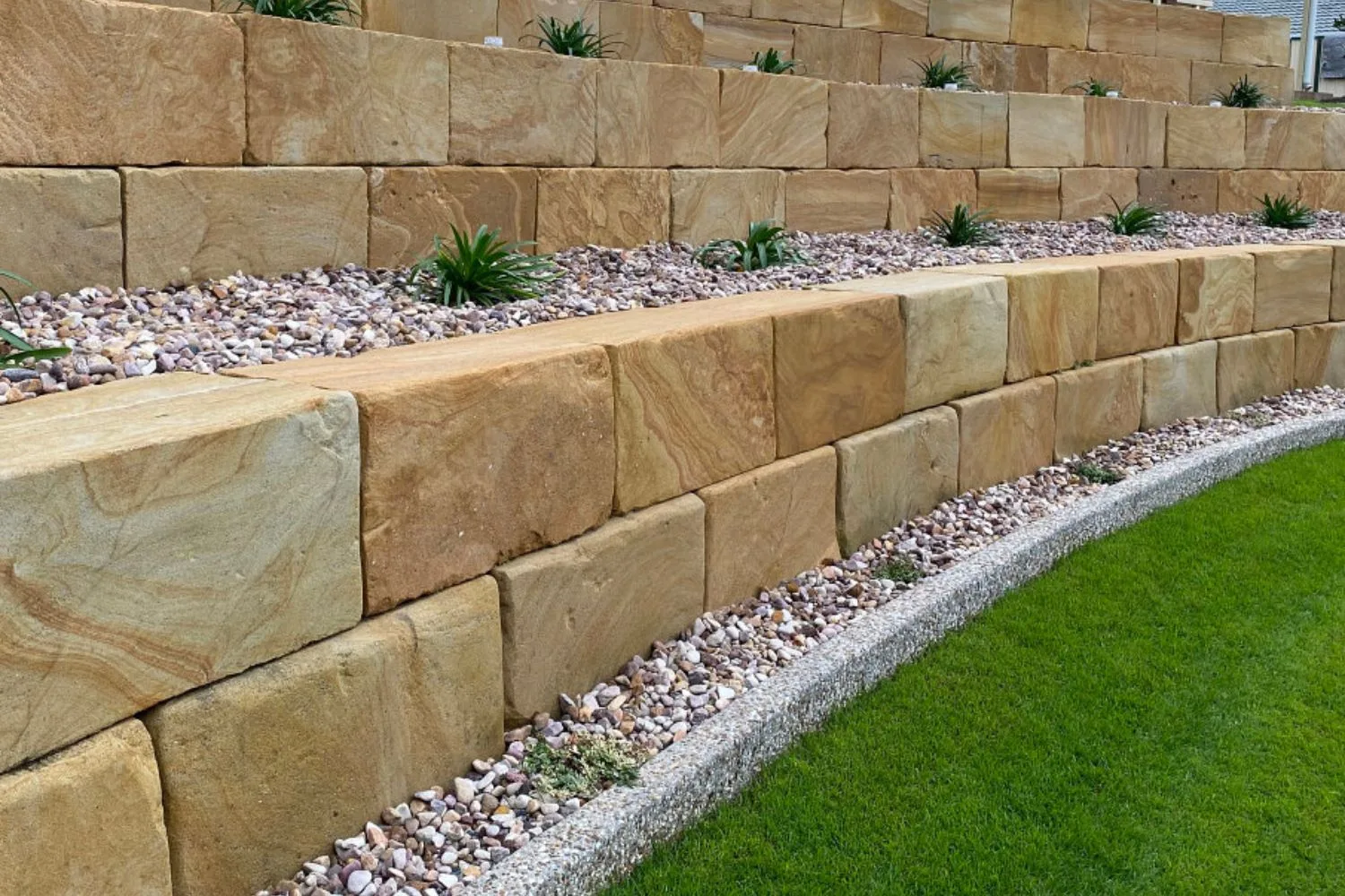 Two-tier sandstone block retaining wall with pebble edging