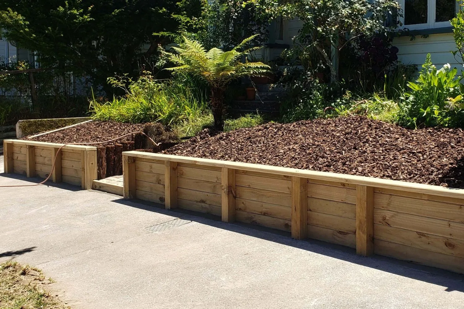 Timber retaining walls edging mulched garden beds beside a driveway